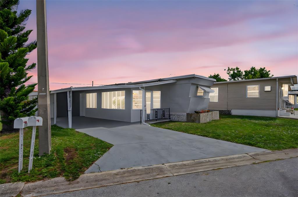 A single-story mobile home with a carport and a concrete driveway at sunset — 5162 BOCA RATON AVENUE, SARASOTA, FL