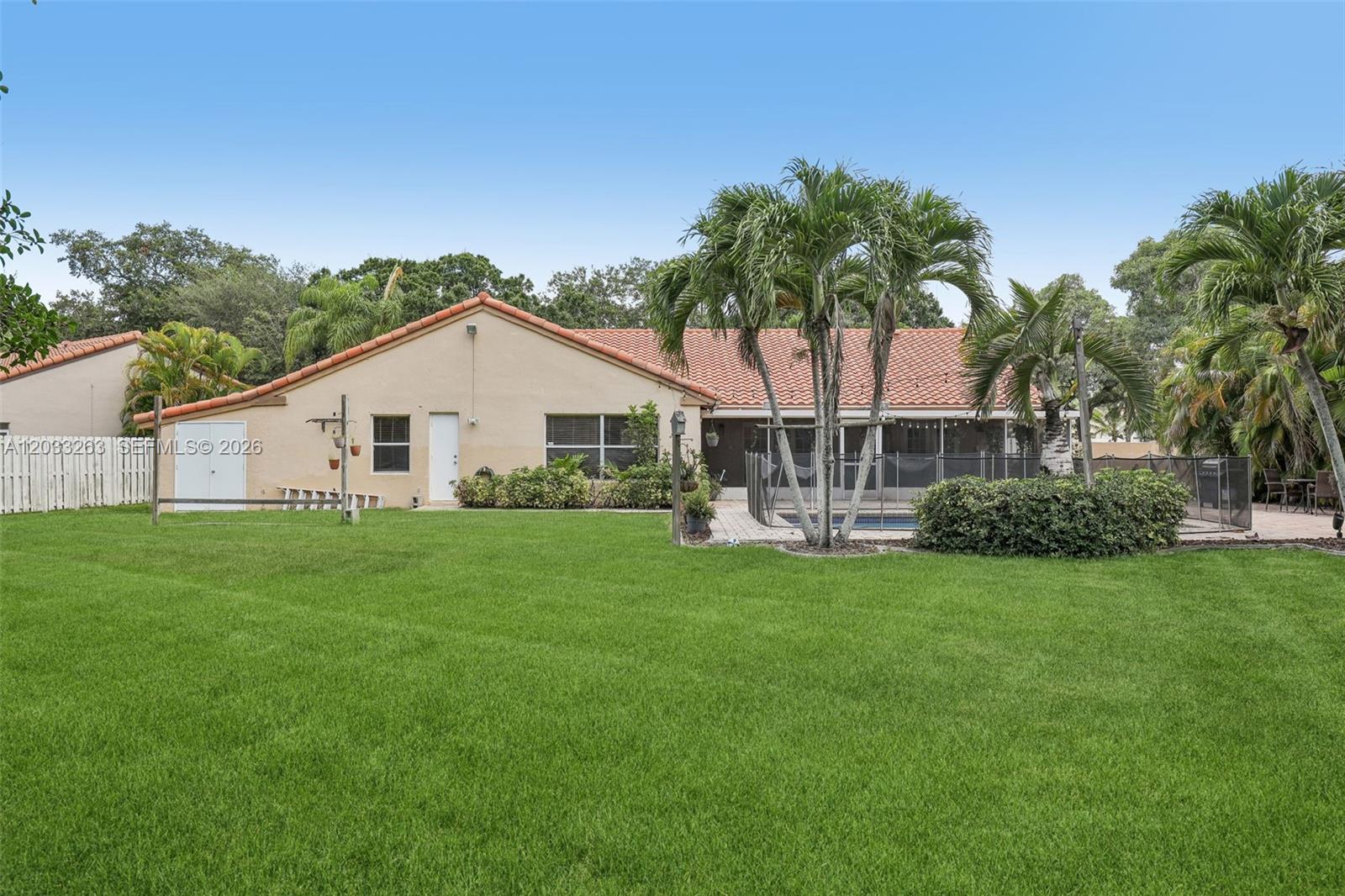 A backyard features a tan house with a tiled roof, a pool, and palm trees — 13100 NW 11th Dr, Sunrise FL 33323, SUNRISE, FL