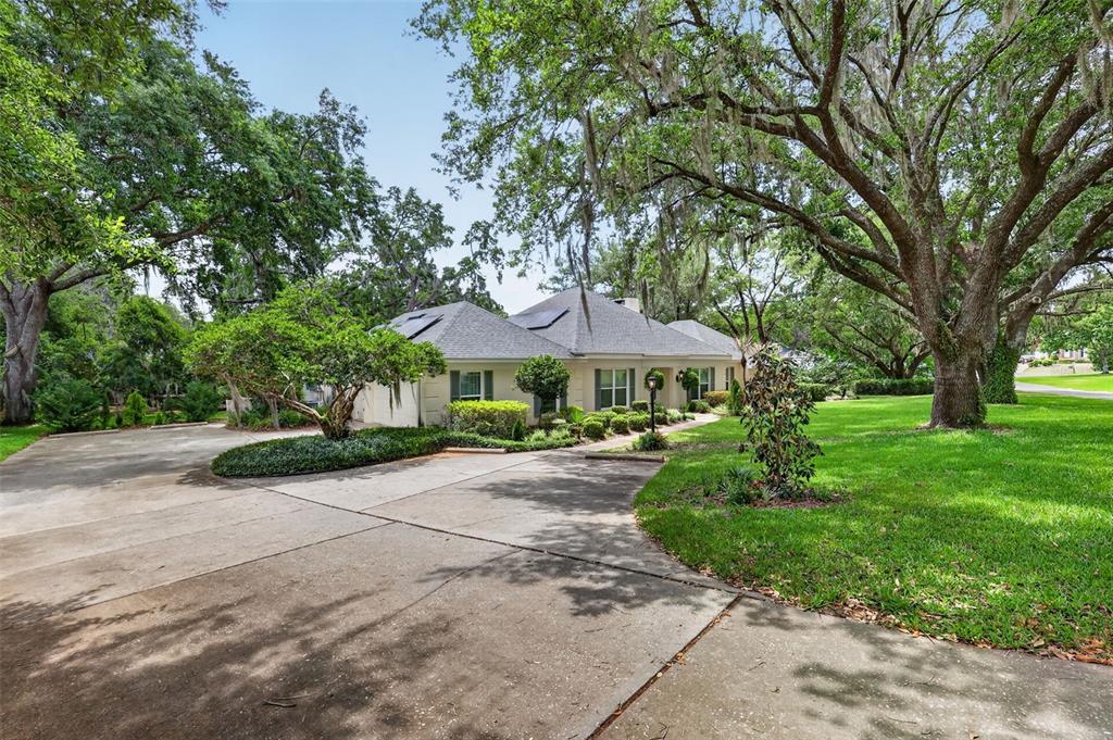 A single-story house with a concrete driveway, surrounded by large trees and a green lawn — 33746 SPRING DRIVE, LEESBURG, FL