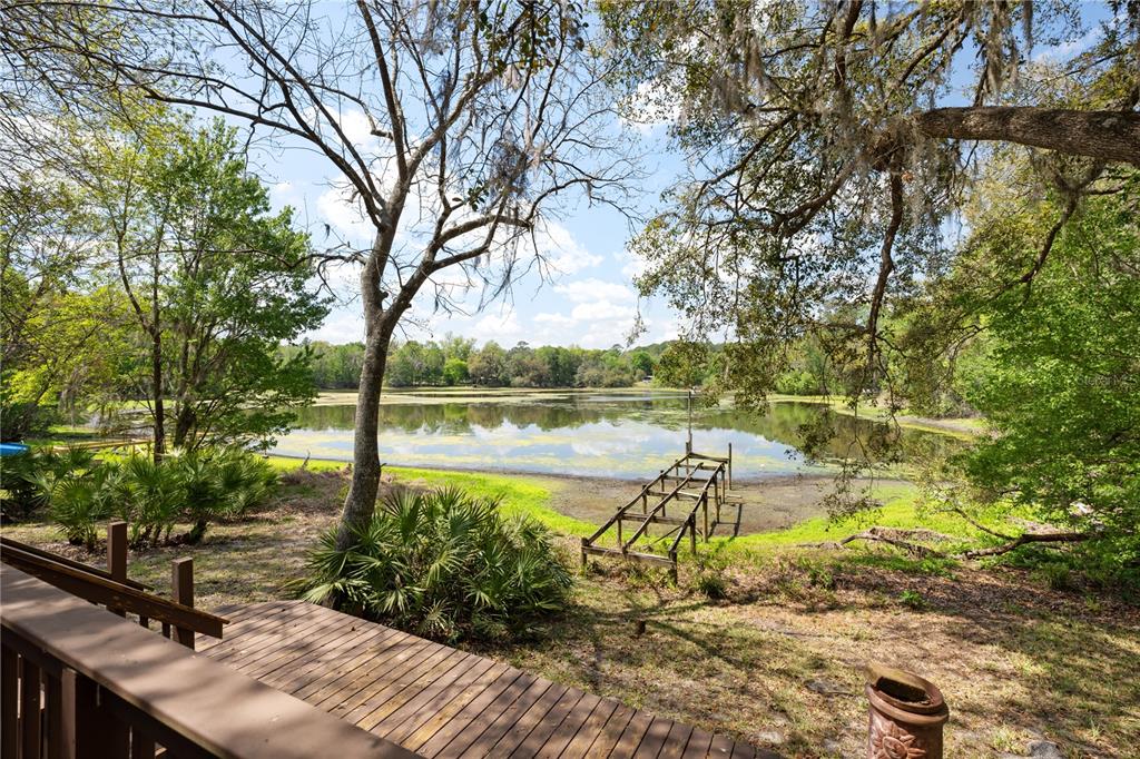 A wooden deck overlooks a grassy yard, a small dock, and a pond surrounded by trees — 2550 SE 31ST STREET, GAINESVILLE, FL