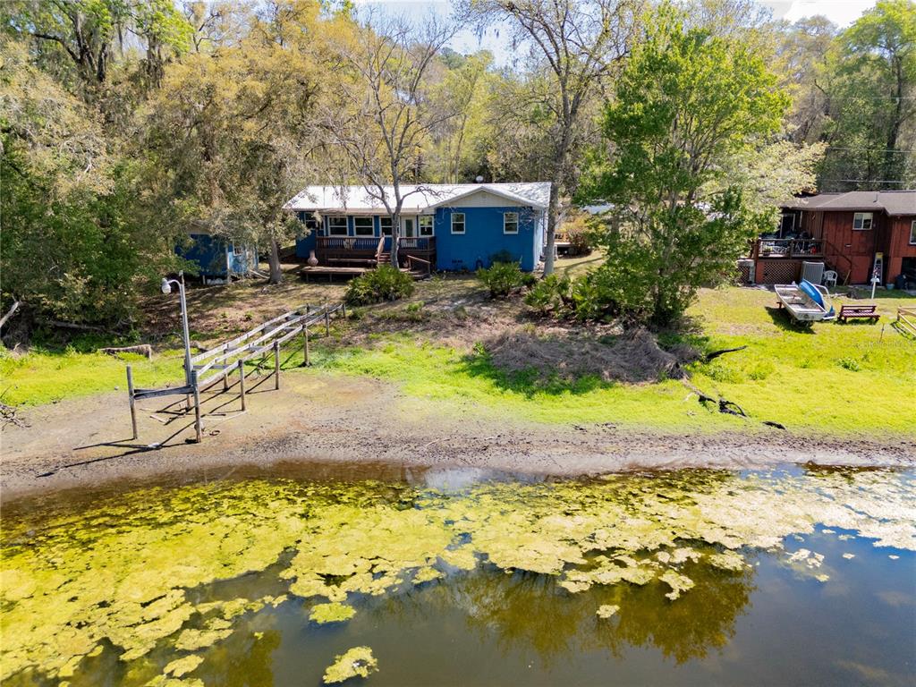 A blue house sits on a grassy bank overlooking a lake with a wooden dock — 2550 SE 31ST STREET, GAINESVILLE, FL