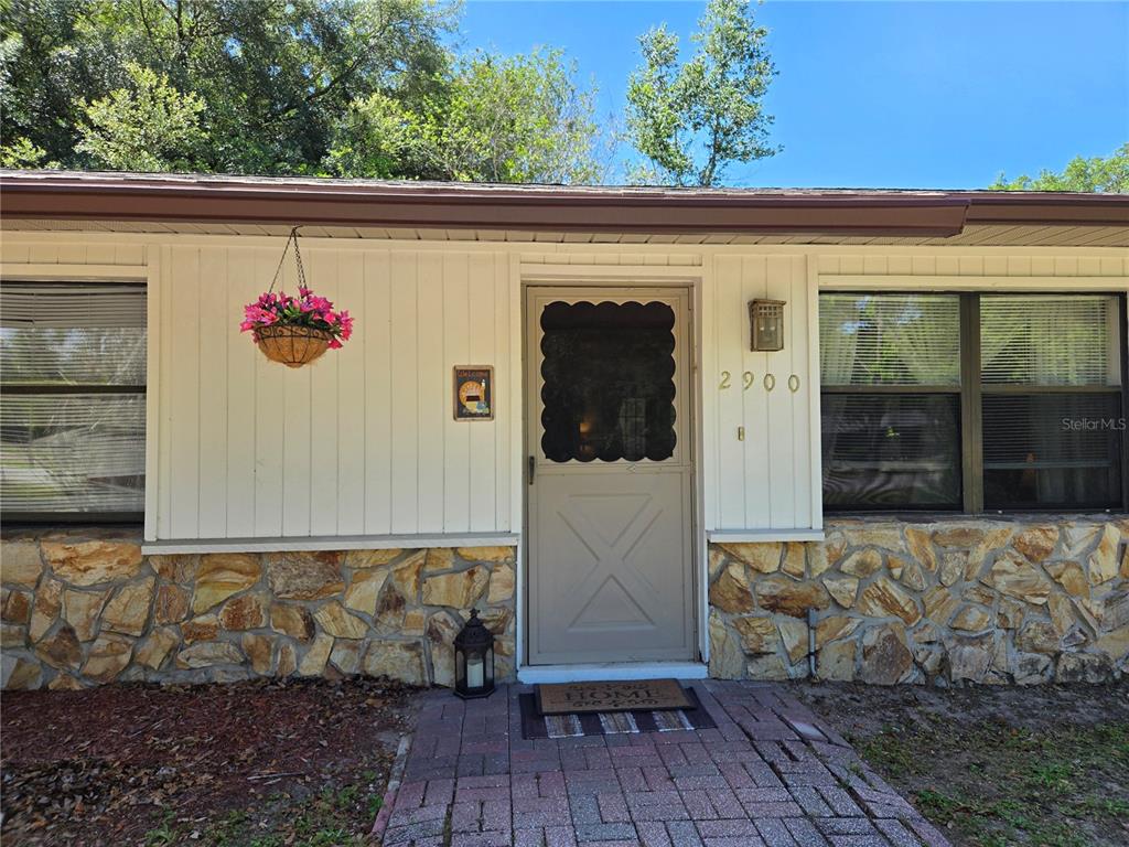 The exterior of a house features a stone base, white vertical siding, and a screen door — 2900 NE 49TH STREET, OCALA, FL