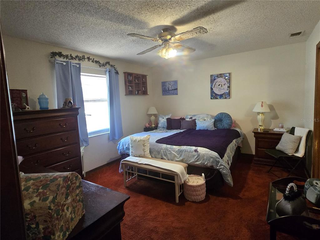 A bedroom features a bed with purple bedding, a wooden dresser, and rust-colored carpeting — 2900 NE 49TH STREET, OCALA, FL