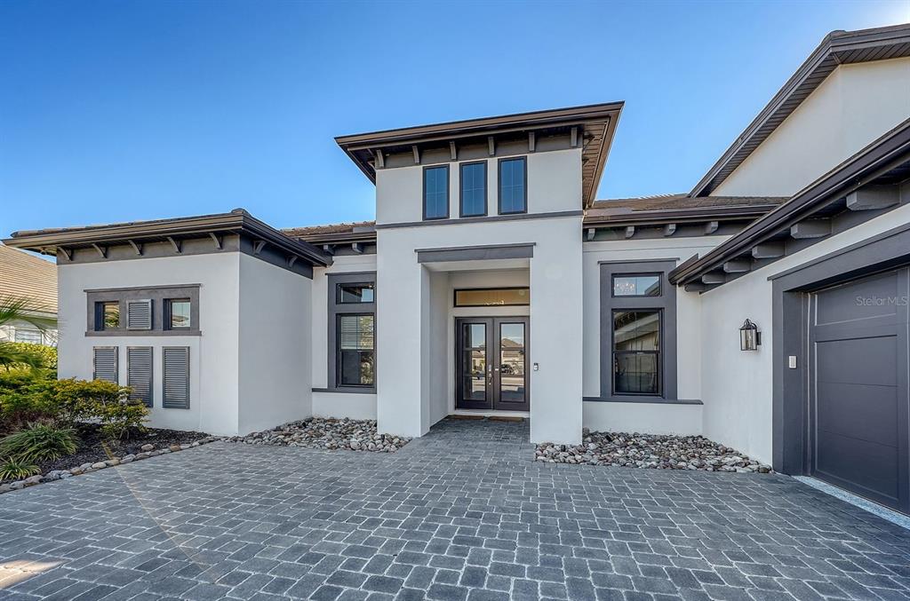 A modern house exterior features white stucco walls, dark trim, and a stone paver driveway — 9296 STARRY NIGHT AVENUE, SARASOTA, FL