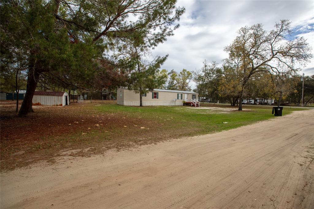 A single-story mobile home sits on a large, grassy lot with trees and a shed — 7160 PURDUE STREET, KEYSTONE HEIGHTS, FL