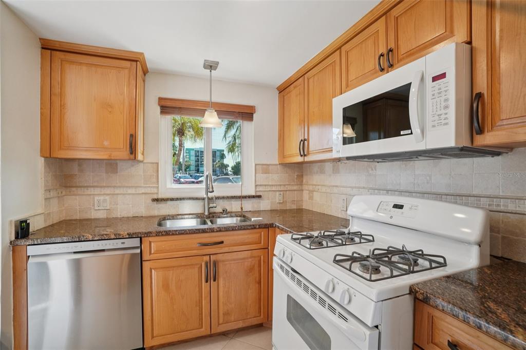 A kitchen with wood cabinets, granite countertops, a stainless steel dishwasher, and a white stove — 1847 SHORE DRIVE S UNIT 117, SOUTH PASADENA, FL