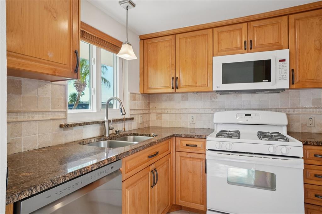 A kitchen features wood cabinets, granite countertops, a white stove, and a stainless steel dishwasher — 1847 SHORE DRIVE S UNIT 117, SOUTH PASADENA, FL