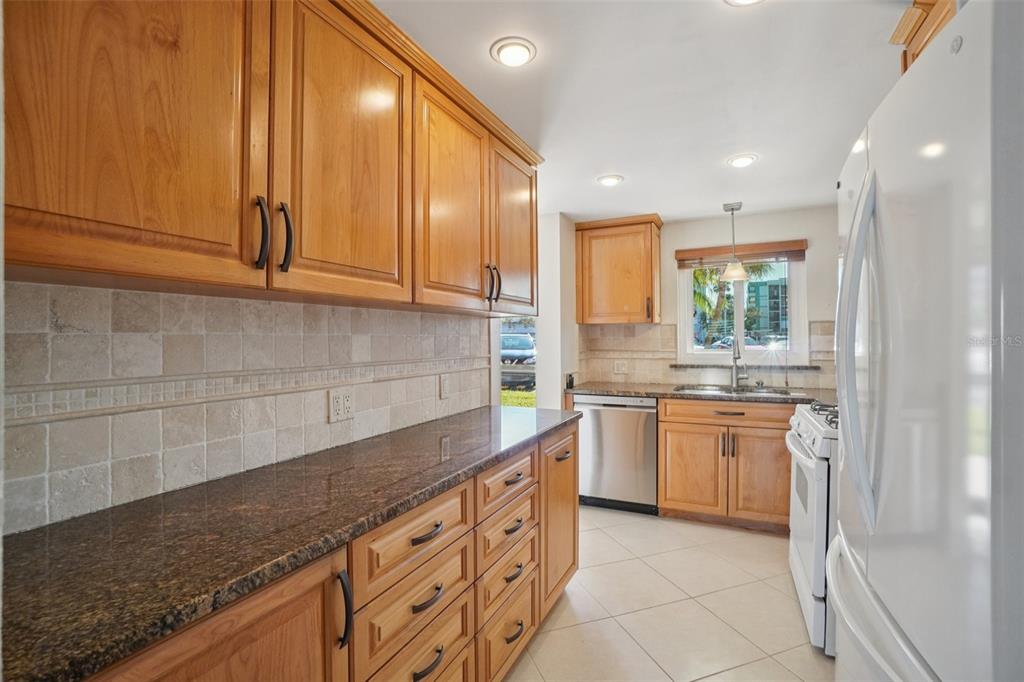 A kitchen with wood cabinets, granite countertops, tile backsplash, and stainless steel appliances — 1847 SHORE DRIVE S UNIT 117, SOUTH PASADENA, FL