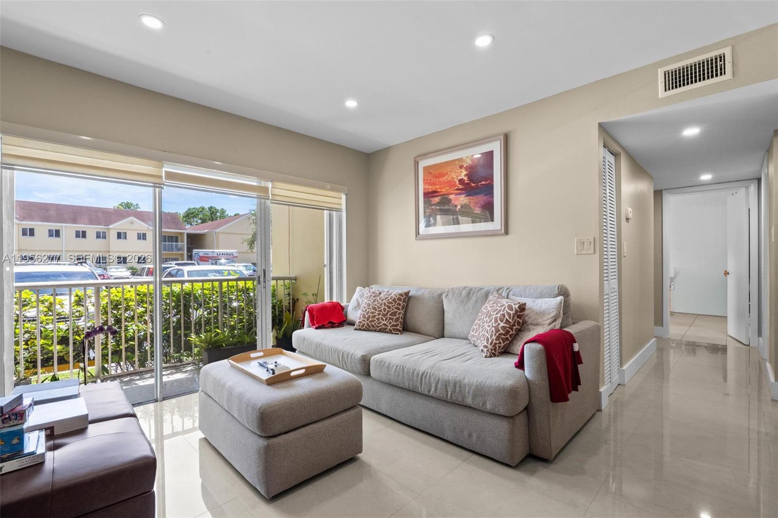 A living room with a gray sofa, ottoman, tile floors, and a sliding glass balcony door — 13810 SW 112th St # 102, Miami FL 33186, MIAMI, FL