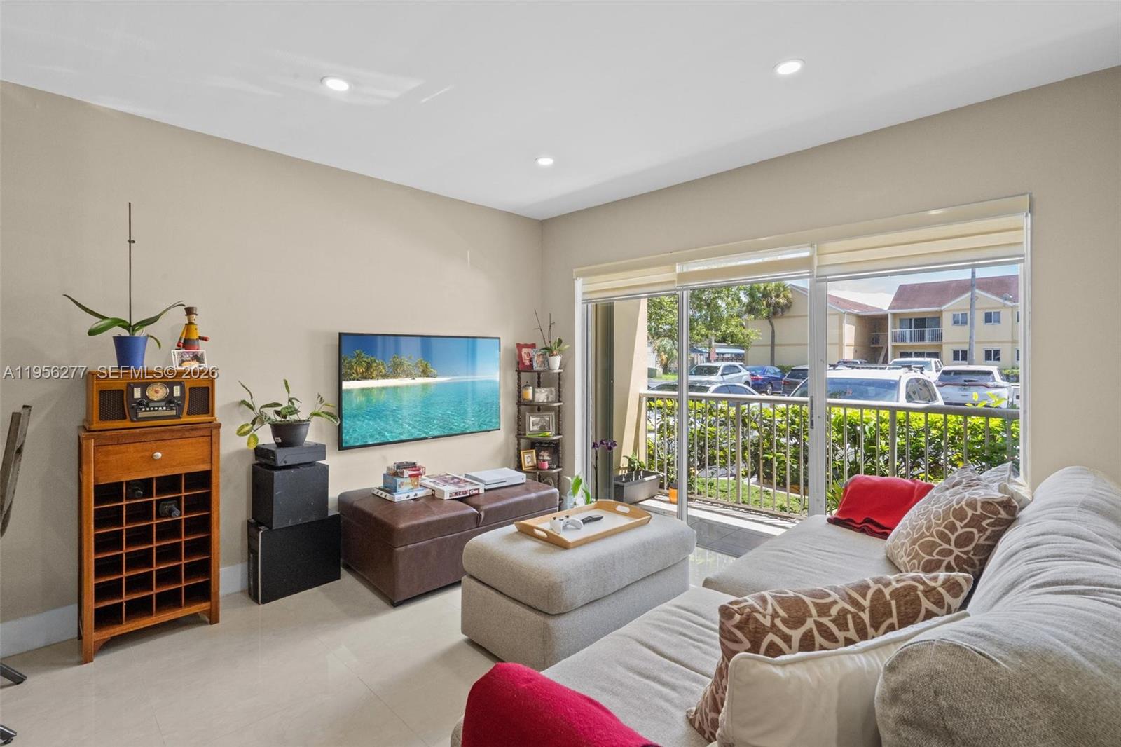 A living room features a wall-mounted television, a sofa, and a sliding glass door balcony — 13810 SW 112th St # 102, Miami FL 33186, MIAMI, FL
