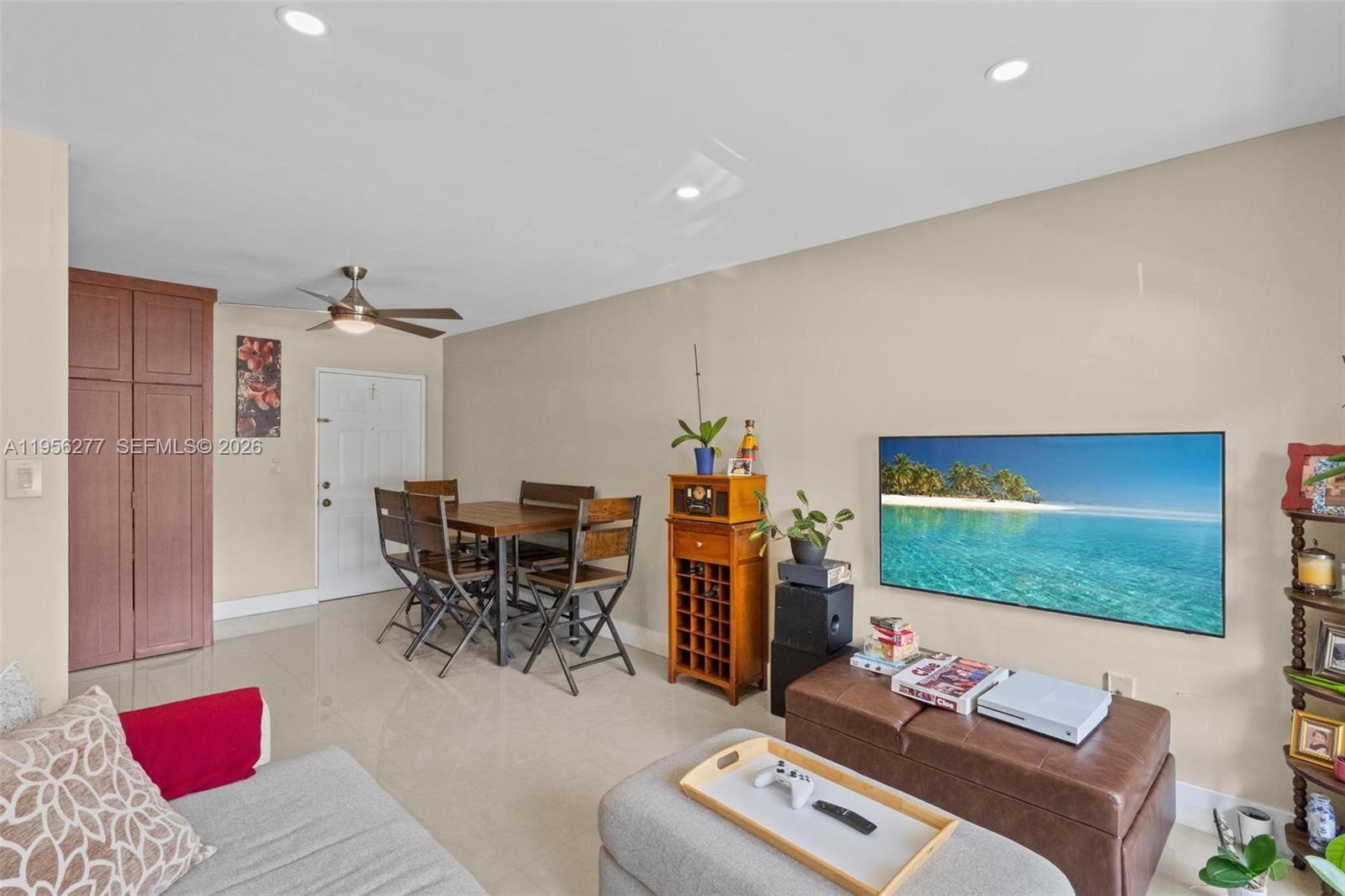 A living room features a wall-mounted television, a dining set, and a brown ottoman — 13810 SW 112th St # 102, Miami FL 33186, MIAMI, FL