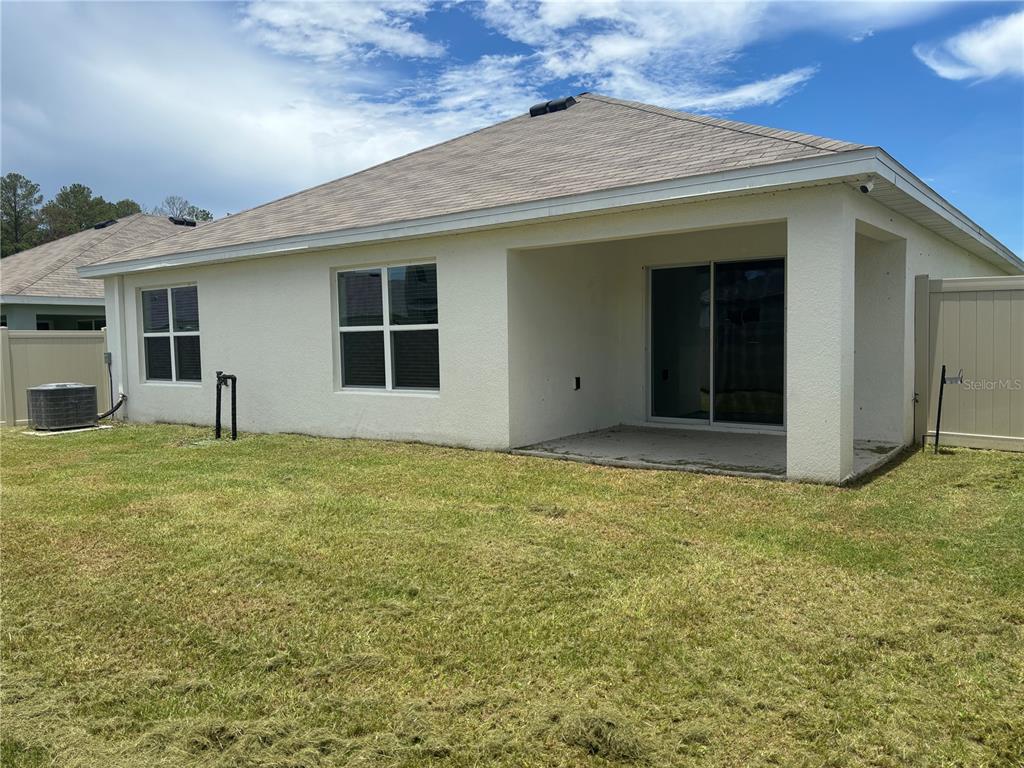 The exterior back view of a house shows a covered patio, sliding doors, and windows — 6670 SE 3RD LOOP, OCALA, FL