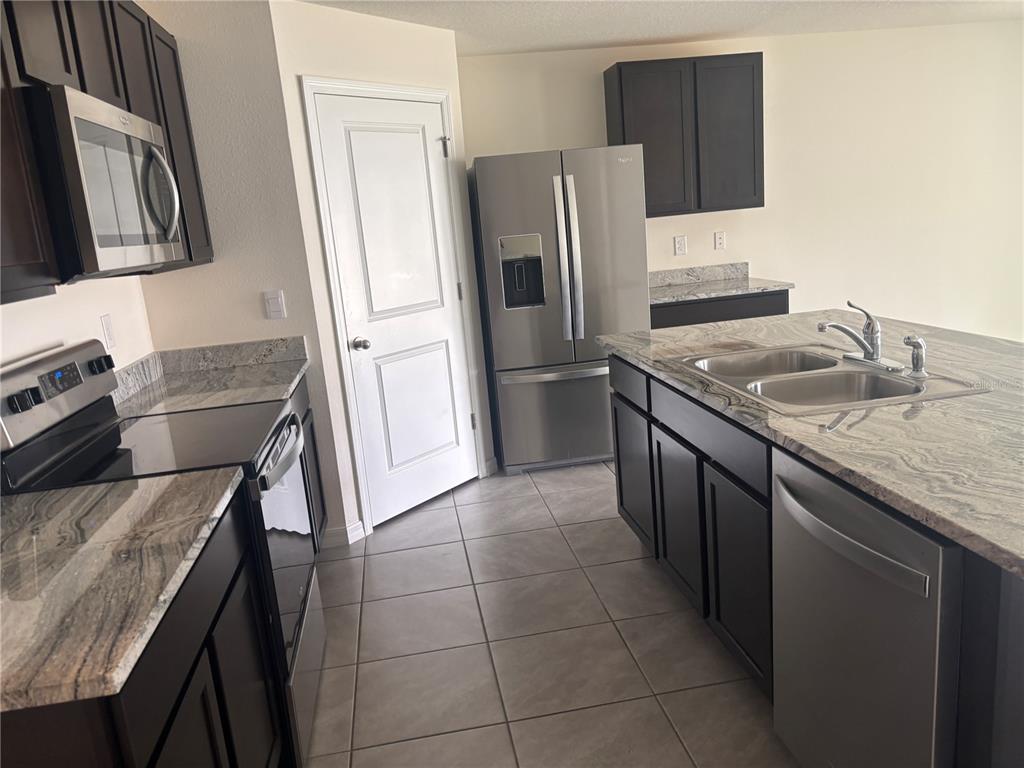 A kitchen features dark wood cabinets, granite countertops, stainless steel appliances, and tile flooring — 6670 SE 3RD LOOP, OCALA, FL