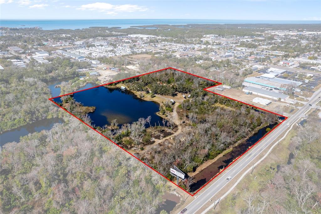 An aerial view shows a large, wooded plot of land featuring a pond and billboard — 8301 CONGRESS STREET, PORT RICHEY, FL