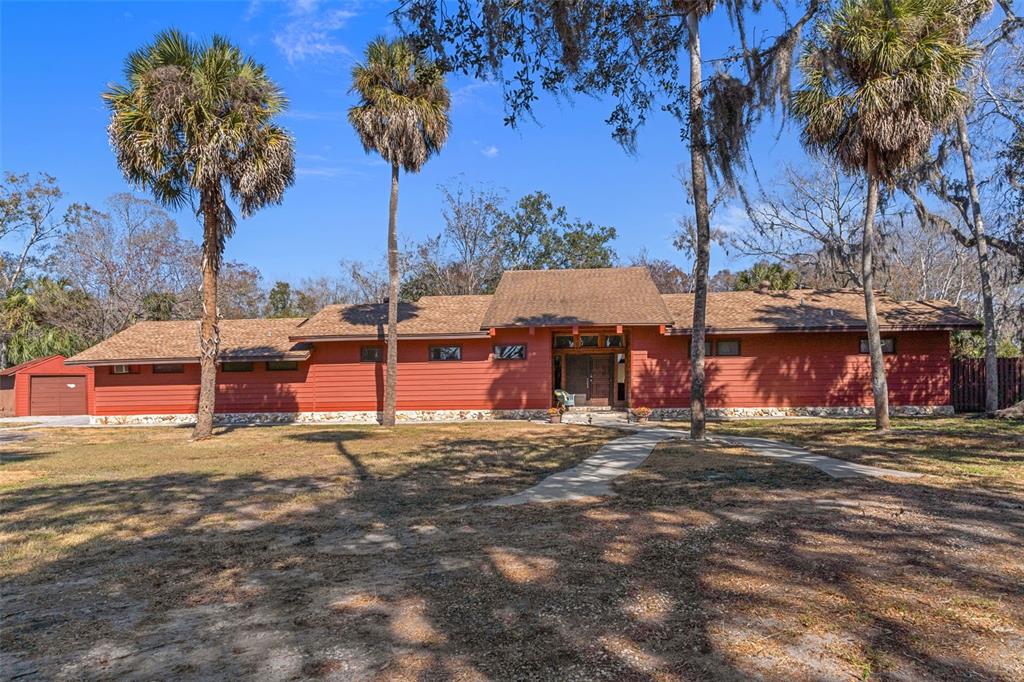 A single-story red house with a brown shingled roof surrounded by palm trees and trees — 8301 CONGRESS STREET, PORT RICHEY, FL