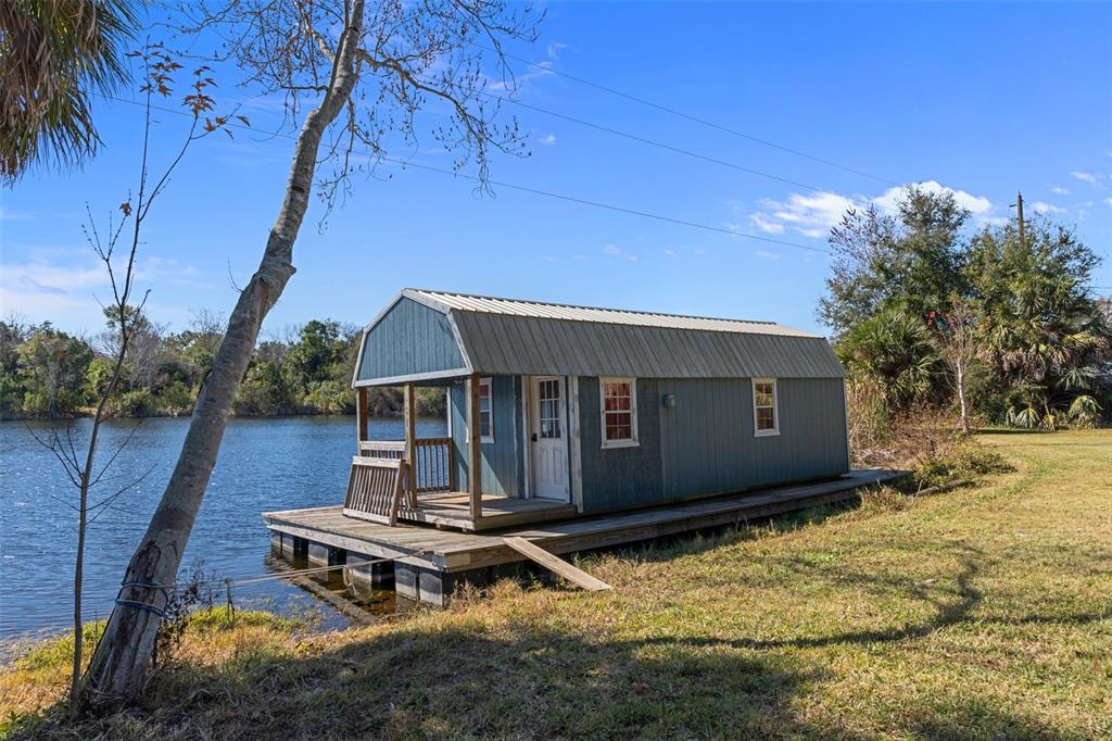 A small blue cabin with a porch sits on a floating dock by a lake — 8301 CONGRESS STREET, PORT RICHEY, FL