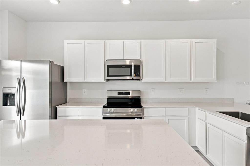 A modern kitchen features white cabinets, stainless steel appliances, and a large quartz-topped island — 2164 RIDER RAIN LANE, APOPKA, FL