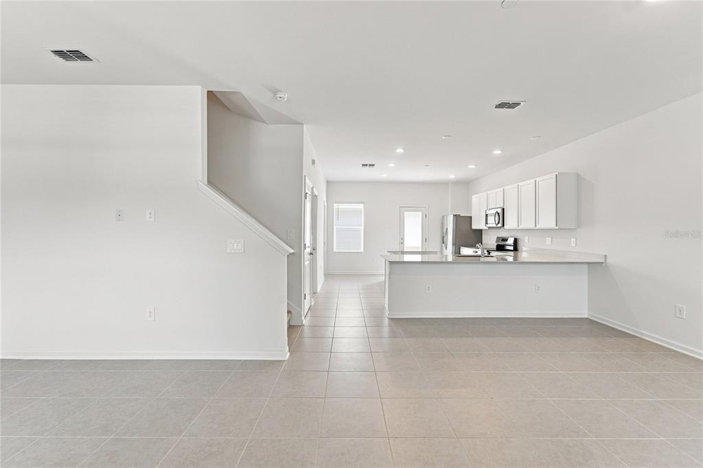 An open-concept kitchen with white cabinets and a breakfast bar overlooks a tiled living area — 2164 RIDER RAIN LANE, APOPKA, FL