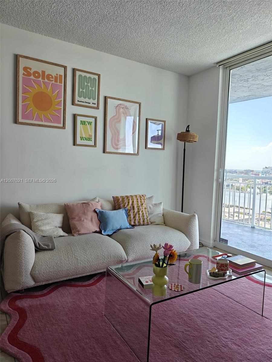 A living room features a cream sofa, a pink wavy rug, and a gallery wall — 275 NE 18th St # 1801, Miami FL 33132, MIAMI, FL