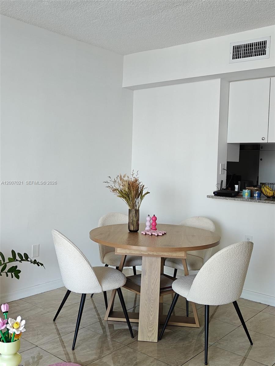 A dining area features a round wooden table with four cream-colored chairs on tiled floors — 275 NE 18th St # 1801, Miami FL 33132, MIAMI, FL