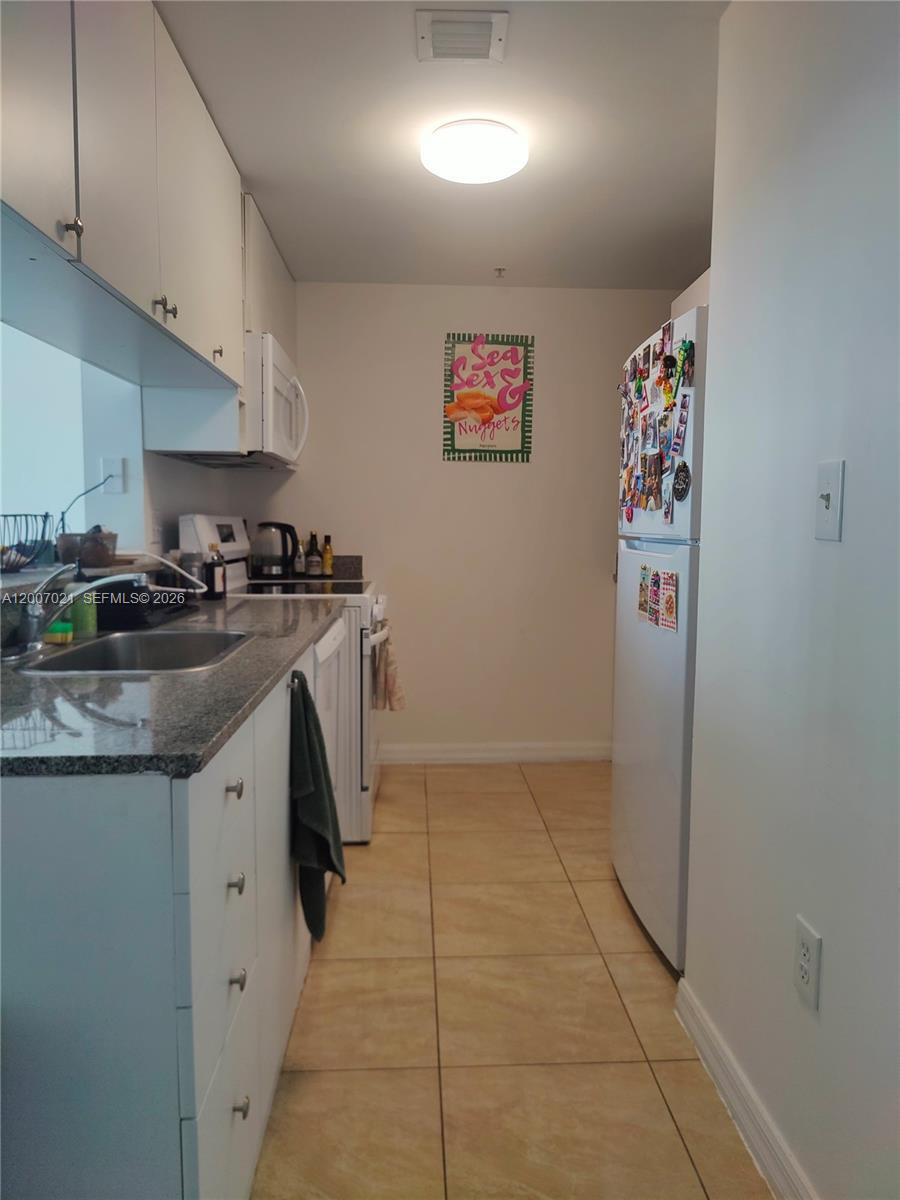 A galley kitchen features white cabinets, granite countertops, a white refrigerator, and tile flooring — 275 NE 18th St # 1801, Miami FL 33132, MIAMI, FL