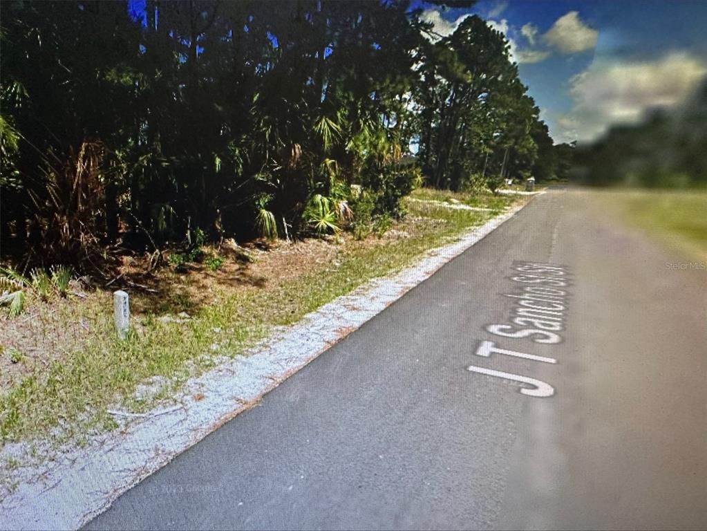 A paved road runs alongside a wooded lot with a small white survey marker — 271 J T SANCHO STREET SW, PALM BAY, FL