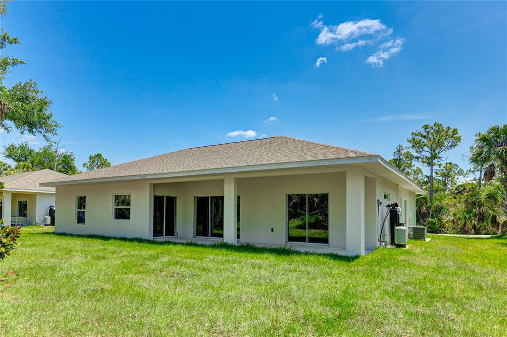 The exterior rear view of a single-story house features a covered patio and lawn — 3717 URIAH STREET, NORTH PORT, FL