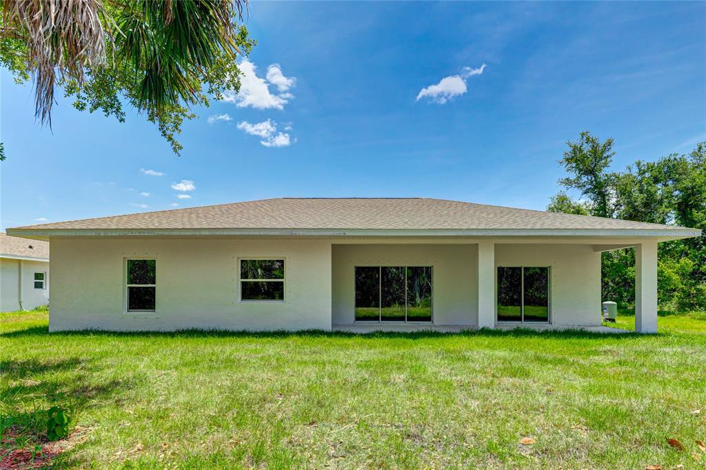 The rear exterior of a single-story house features a covered patio and a grassy yard — 3717 URIAH STREET, NORTH PORT, FL