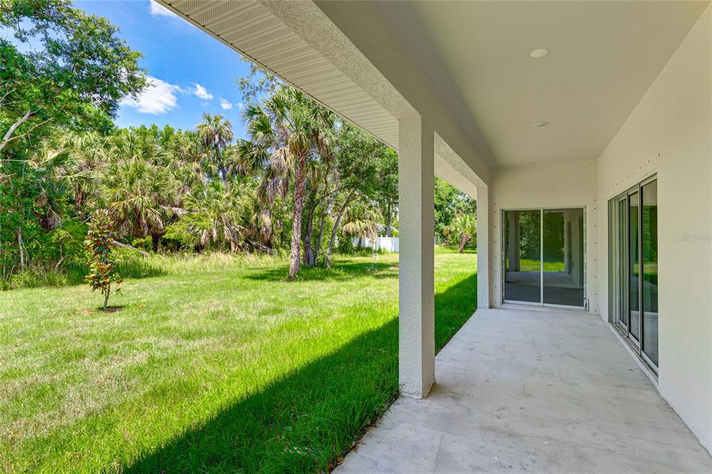 A covered concrete patio overlooks a grassy backyard with trees and palm foliage — 3717 URIAH STREET, NORTH PORT, FL