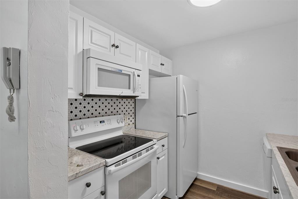A kitchen features white cabinets, a microwave, a stove, a refrigerator, and patterned backsplash tile — 4000 SW 23RD STREET UNIT 1-101, GAINESVILLE, FL