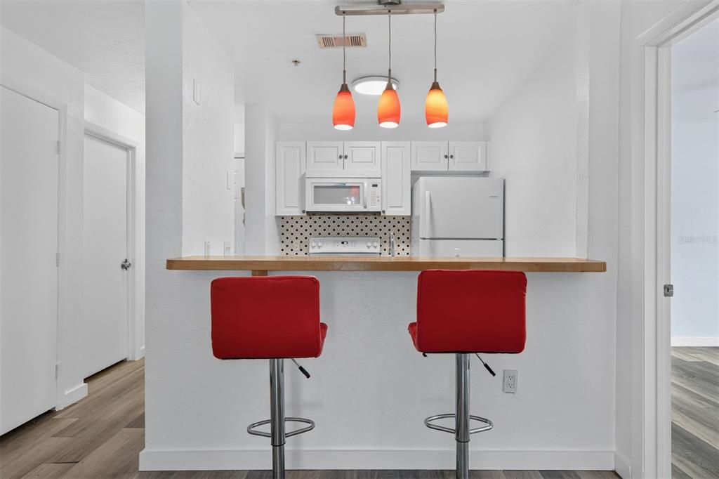 A kitchen features white cabinets, a breakfast bar with two red stools, and pendant lighting — 4000 SW 23RD STREET UNIT 1-101, GAINESVILLE, FL
