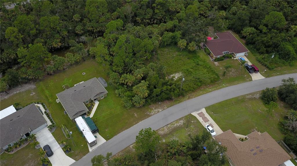An aerial view shows several houses and a vacant wooded lot along a paved road — BASKET STREET, NORTH PORT, FL