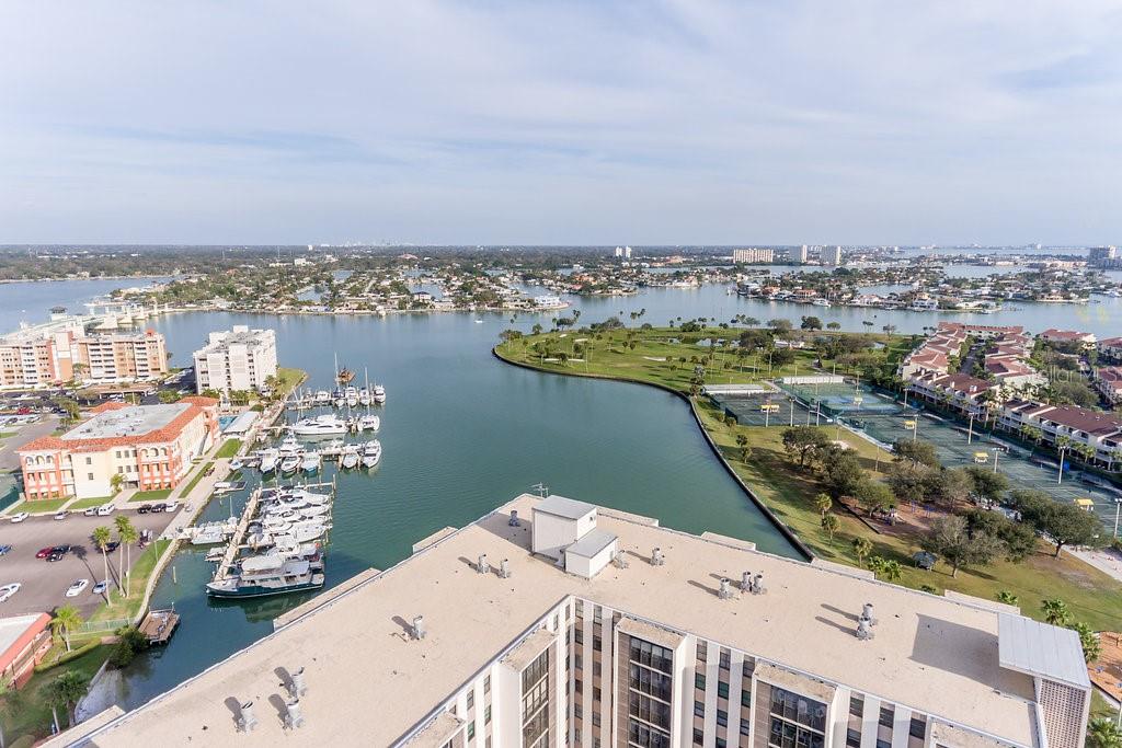 An aerial view shows a high-rise building overlooking a marina, a golf course, and water — 10355 PARADISE BOULEVARD UNIT 103, TREASURE ISLAND, FL