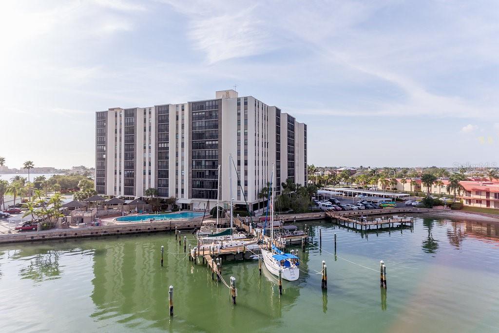 An aerial view of a multi-story apartment building situated on a waterfront with boat docks — 10355 PARADISE BOULEVARD UNIT 103, TREASURE ISLAND, FL