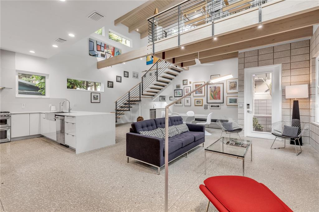 A modern open-concept living room and kitchen with high ceilings, a staircase, and terrazzo flooring — 210 FLORIDA AVENUE, NEW SMYRNA BEACH, FL