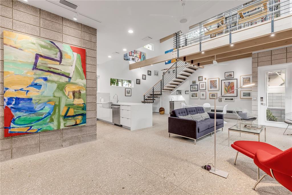 A modern open-concept living room features a large abstract painting, concrete block walls, and stairs — 210 FLORIDA AVENUE, NEW SMYRNA BEACH, FL