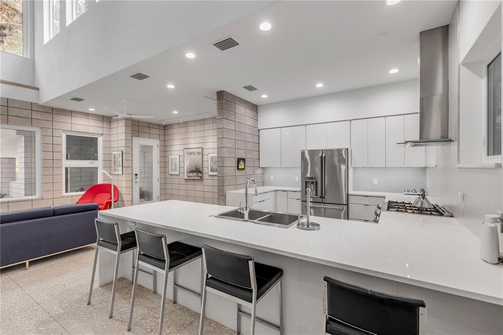 A modern kitchen features white cabinetry, a large quartz island, and exposed concrete block walls — 210 FLORIDA AVENUE, NEW SMYRNA BEACH, FL