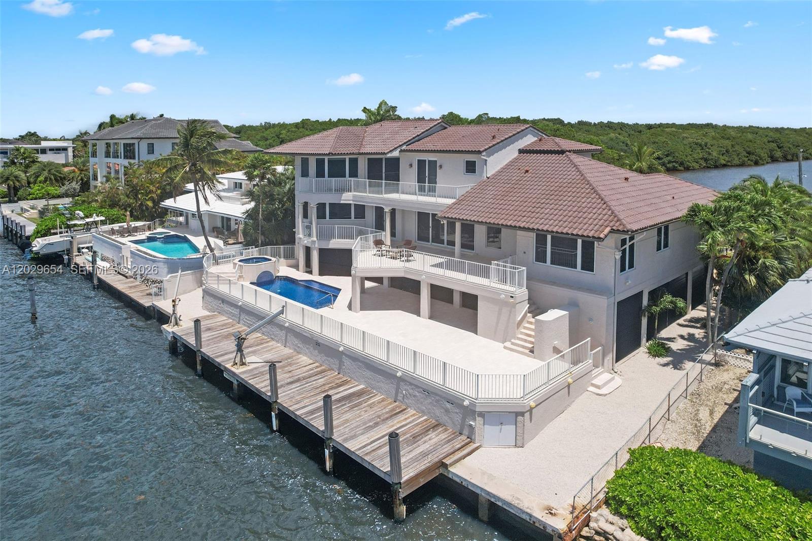 An aerial view of a multi-story waterfront house with a pool, deck, and wooden dock — 750 Lugo Ave, Coral Gables FL 33156, CORAL GABLES, FL
