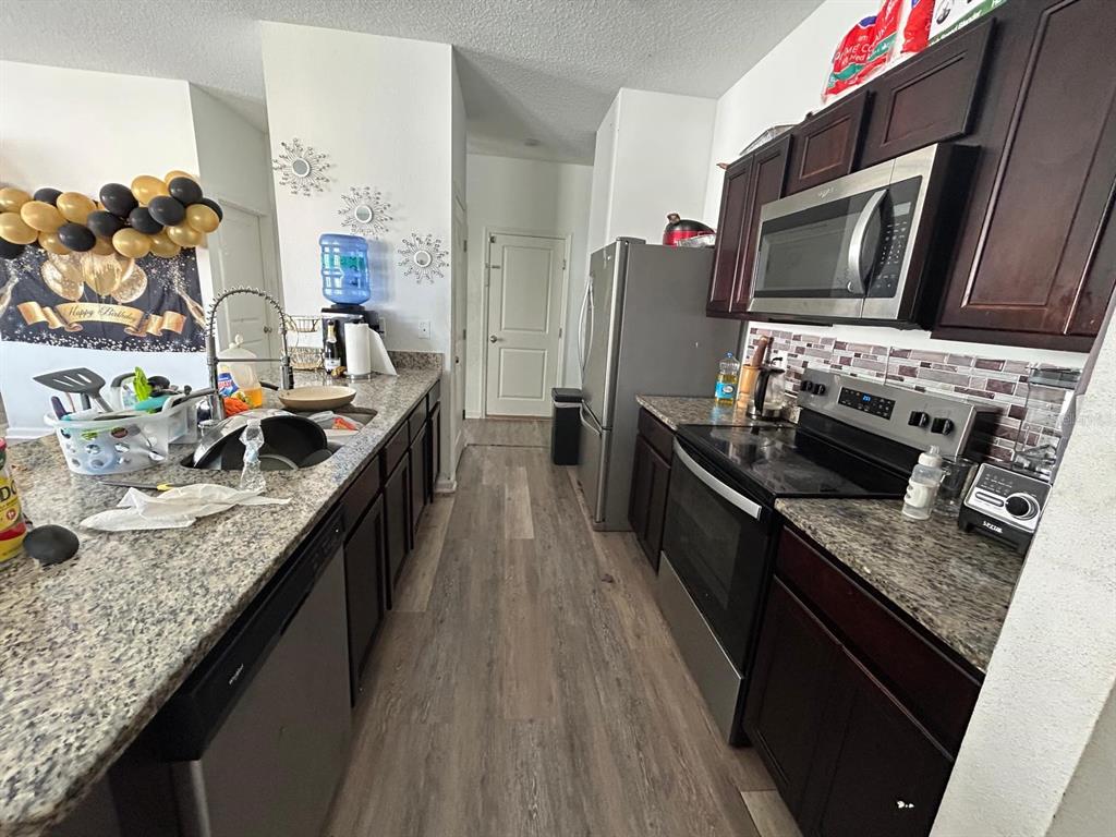 A kitchen features dark wood cabinets, granite countertops, stainless steel appliances, and wood-look flooring — 805 ORCHID GROVE BOULEVARD, DAVENPORT, FL