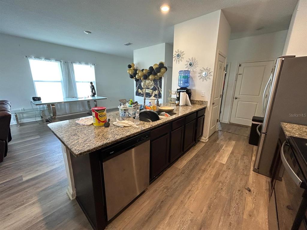 A kitchen features dark wood cabinets, granite countertops, stainless steel appliances, and wood-look flooring — 805 ORCHID GROVE BOULEVARD, DAVENPORT, FL