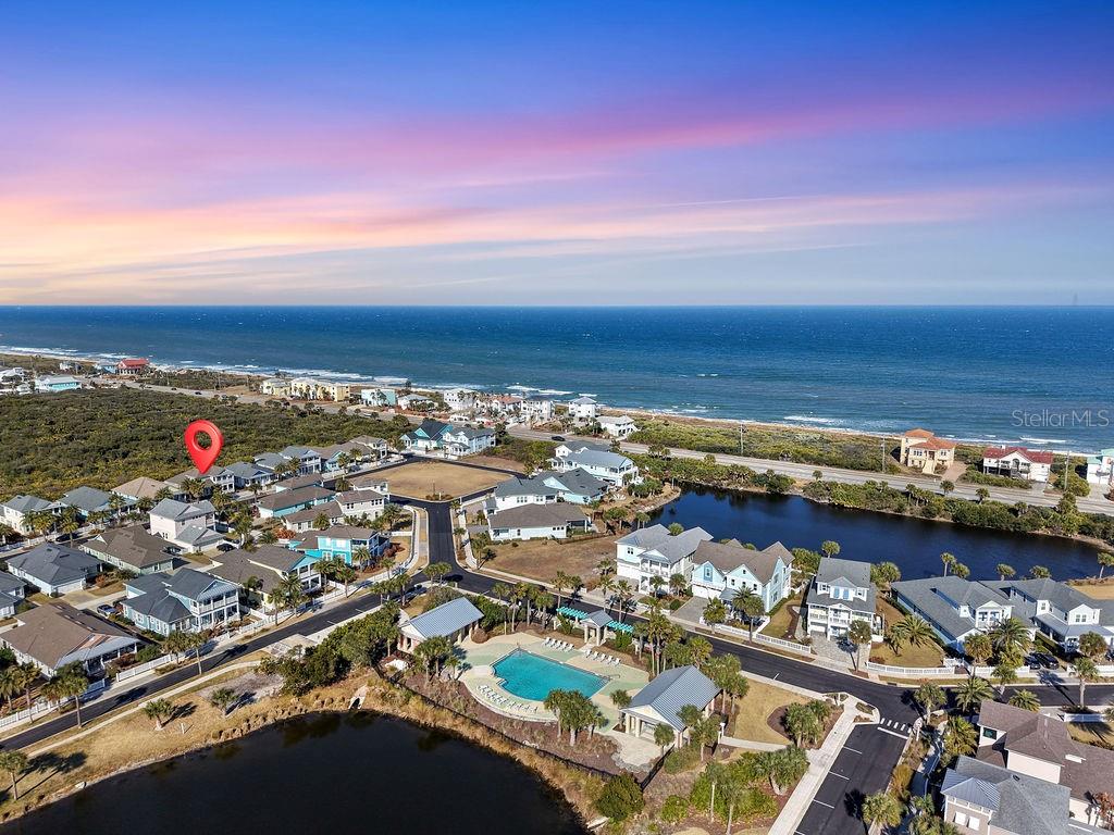 An aerial view shows a coastal neighborhood with houses, a community pool, and the ocean — 4 HIDDEN TREASURE DRIVE, PALM COAST, FL