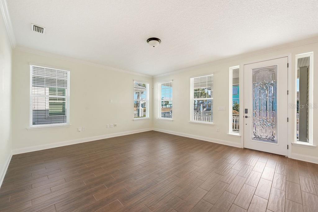 An empty room with wood-look tile flooring, white walls, multiple windows, and a glass-paneled front door — 4 HIDDEN TREASURE DRIVE, PALM COAST, FL