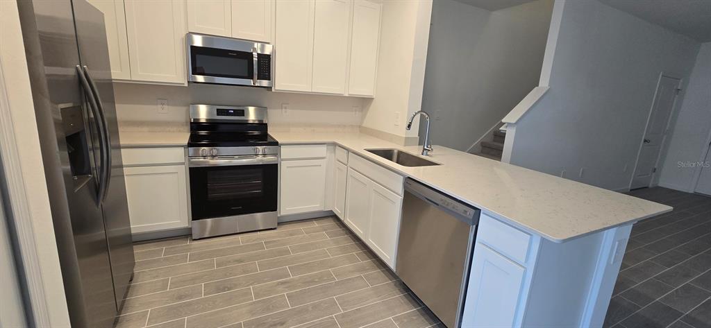 A modern kitchen features white cabinets, stainless steel appliances, and a quartz-topped island — 3577 SE 37 COURT, OCALA, FL