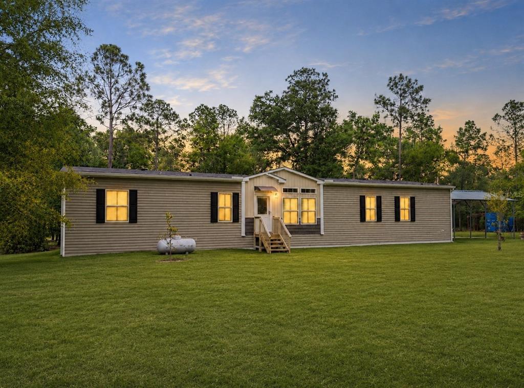 A single-story manufactured home with tan siding sits on a large grassy lot at dusk — 11160 NW 5TH AVENUE, BRANFORD, FL