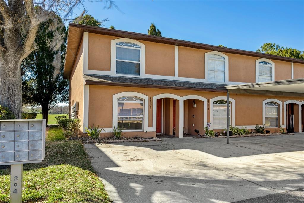 A two-story tan townhouse with arched windows and a concrete driveway with a carport — 14902 PAR CLUB CIRCLE, TAMPA, FL