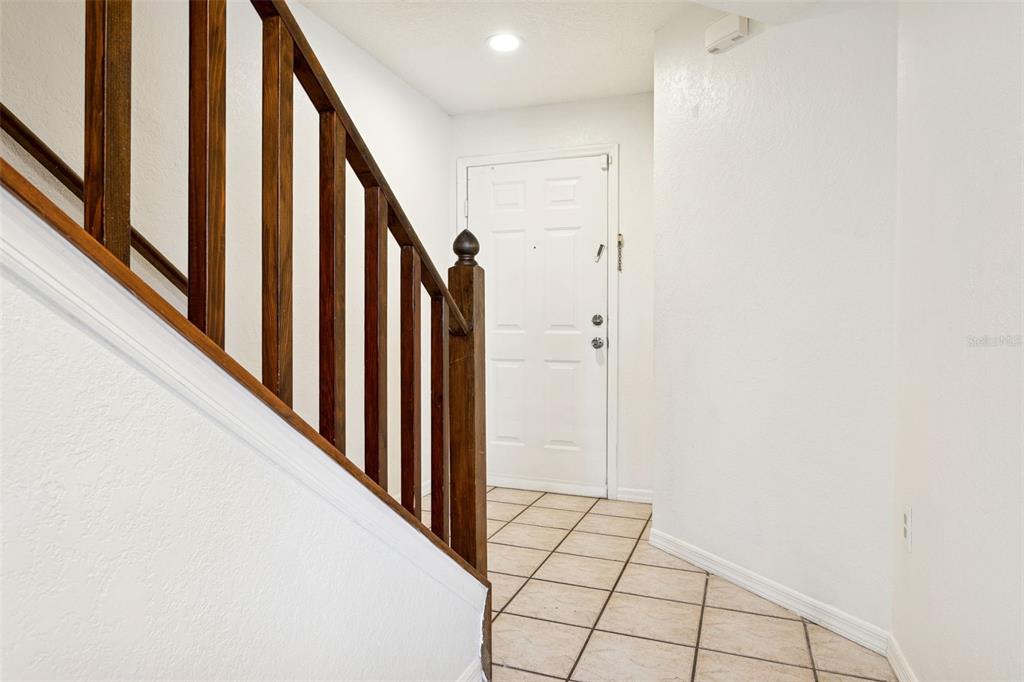 A tiled entryway features a wooden staircase with a railing leading to a white door — 14902 PAR CLUB CIRCLE, TAMPA, FL
