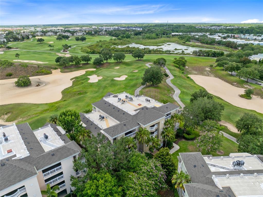An aerial view shows multi-story residential buildings situated next to a golf course and pond — 1360 CENTRE COURT RIDGE DRIVE UNIT 201, REUNION, FL