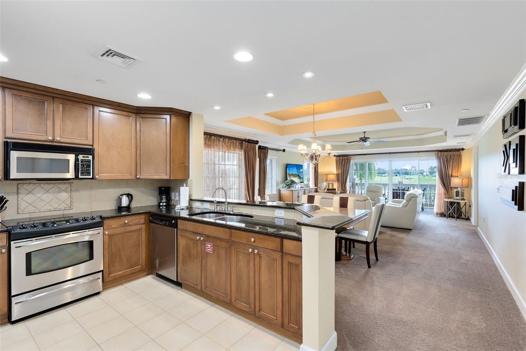 A kitchen with wood cabinets and granite countertops overlooks an open-concept living and dining area — 1360 CENTRE COURT RIDGE DRIVE UNIT 201, REUNION, FL
