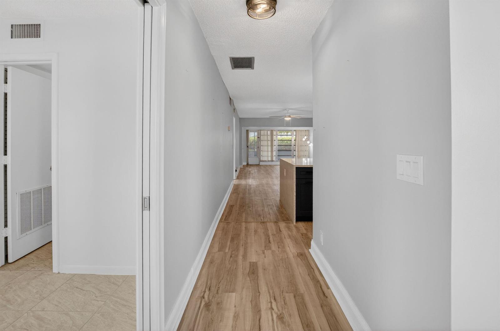 A hallway with light wood-look flooring leads toward a kitchen and a bright living area — 2401 Del Aire Boulevard # 101, Delray Beach FL 33445, DELRAY BEACH, FL