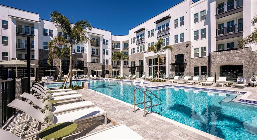 A modern apartment complex courtyard features a swimming pool surrounded by lounge chairs and palm trees — 700 AULTMAN STREET UNIT Heritage, KISSIMMEE, FL